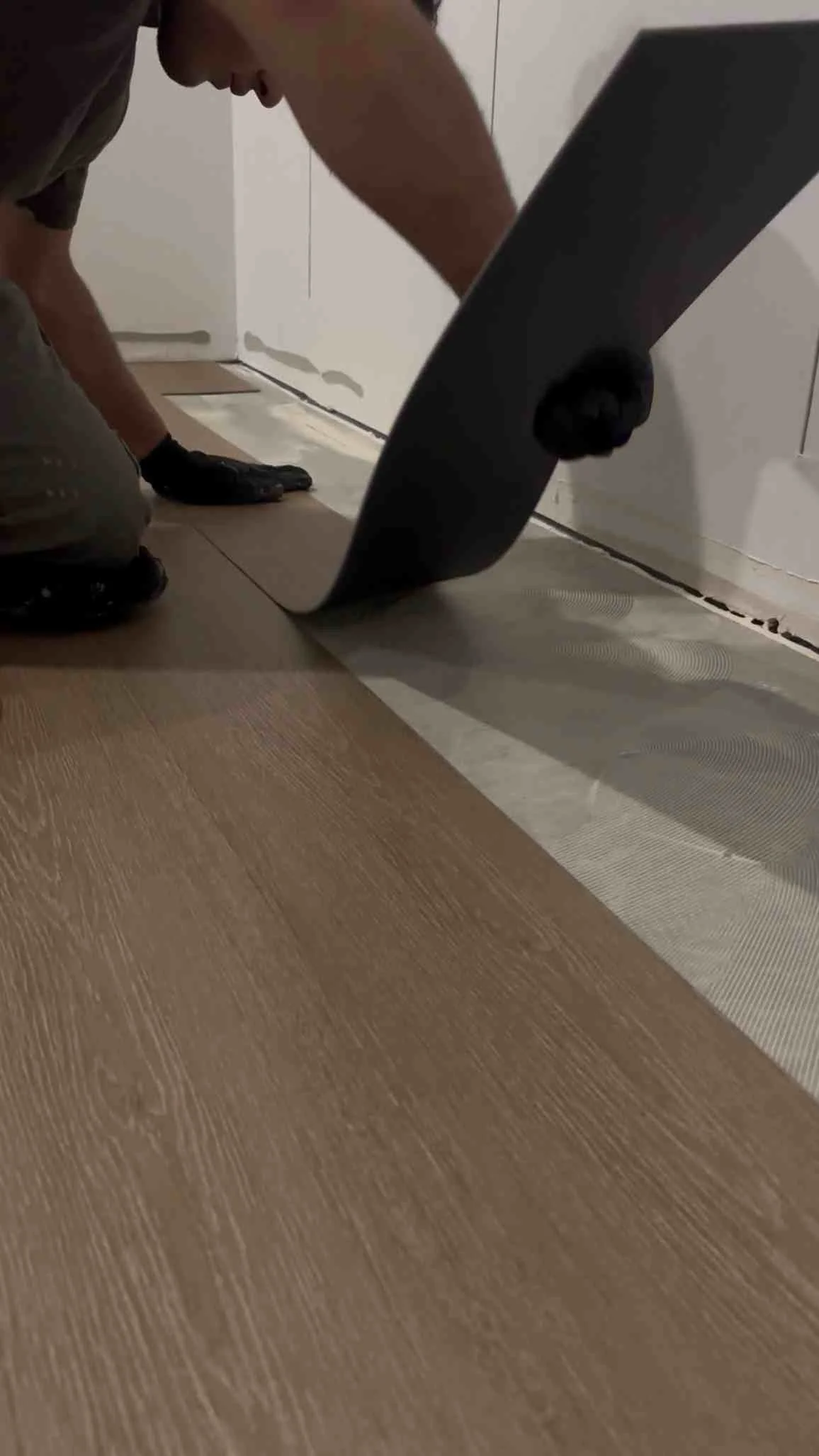 Worker installing luxury vinyl plank flooring with baseboard trim and transition strips Worker installing luxury vinyl plank flooring with baseboard trim and transition strips
